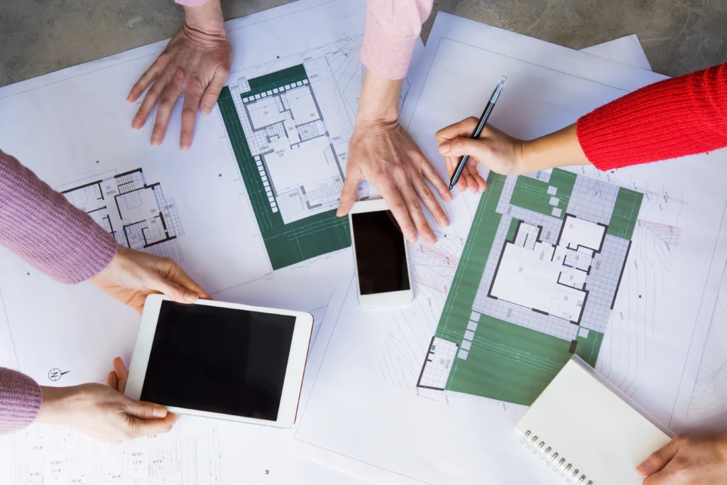 Équipe travaillant sur des plans de maison modernes avec tablettes numériques pour optimiser un financement immobilier à Basse-Goulaine