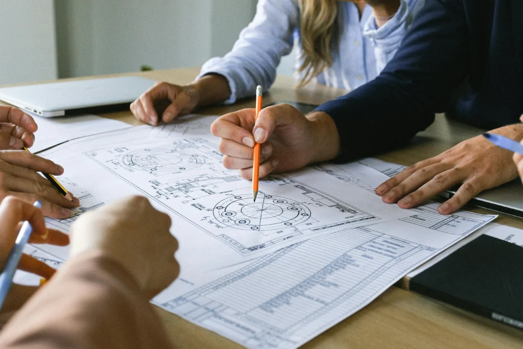 Réunion de travail entre un courtier à Bruz et ses clients, pointant des détails techniques sur un plan de construction pour valider le financement