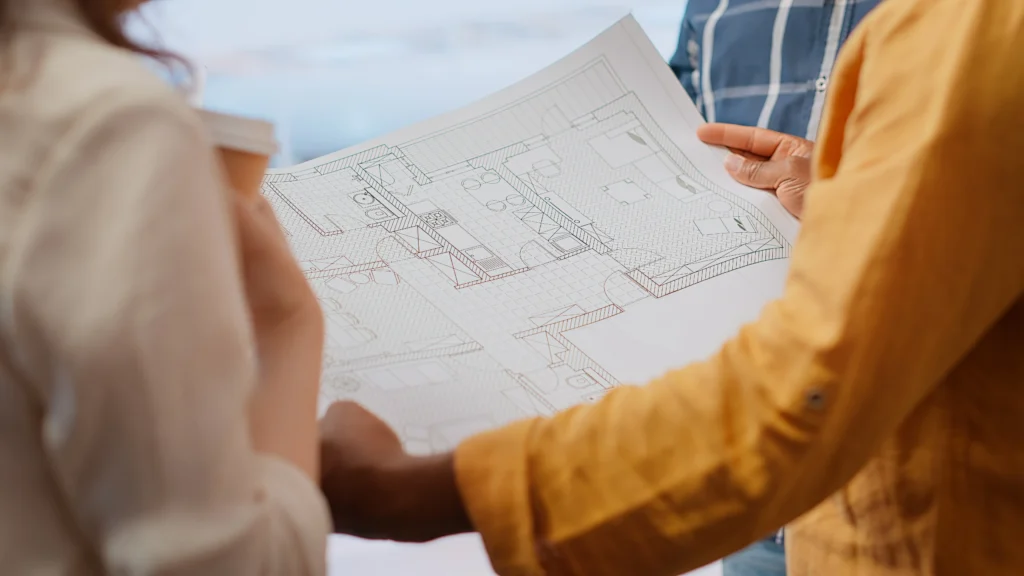 Couple et courtier immobilier consultant les plans d'une maison lors d'une visite pour valider un financement à Dol-de-Bretagne