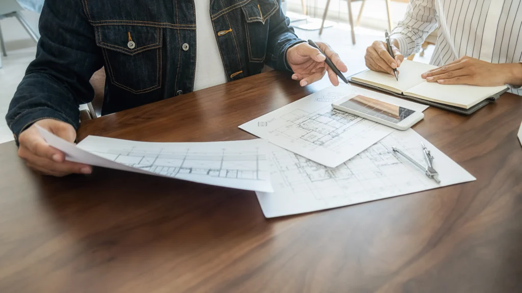 Réunion de travail entre un courtier et ses clients à Saint-Herblain, utilisant plans et outils numériques pour affiner une stratégie de financement.